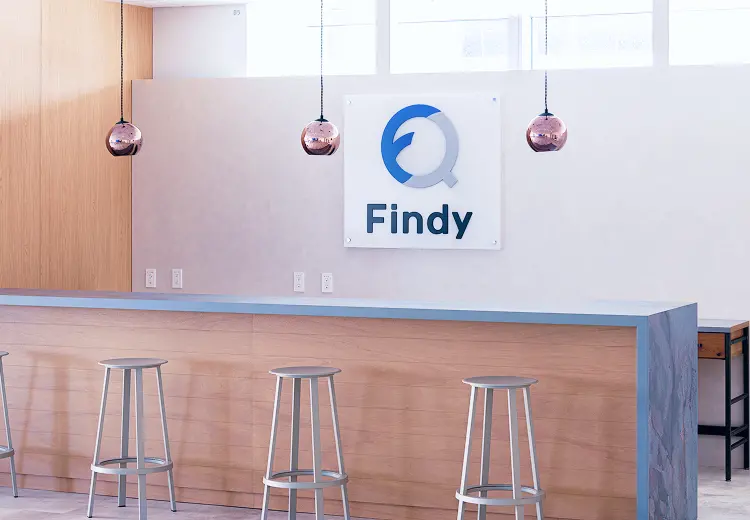 ウッド調のカウンターとブルーのアクセント、銅色のペンダントライトが調和した、Findyロゴが映えるカフェカウンター