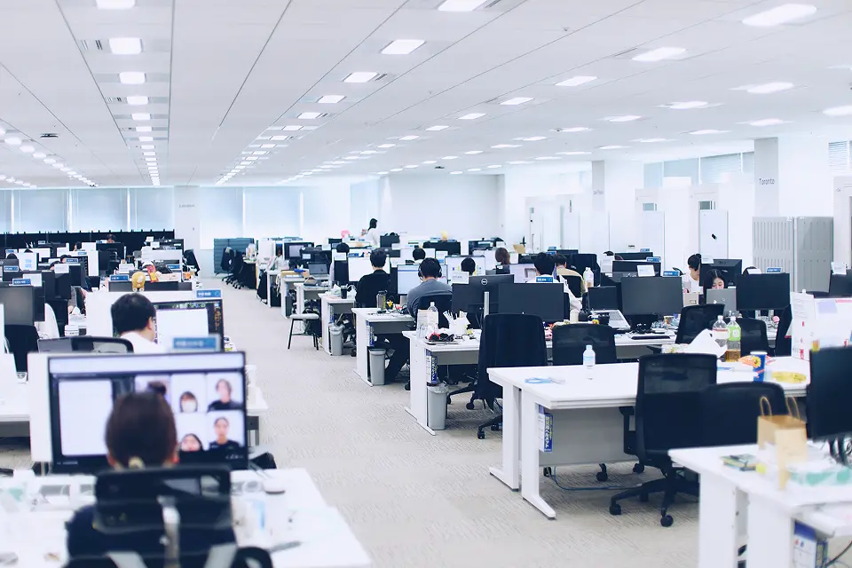 白を基調とした明るく広々とした執務室。整然と並ぶデスクでリモートミーティングや業務に取り組む社員の様子が見える、クリーンで開放的なオフィス環境